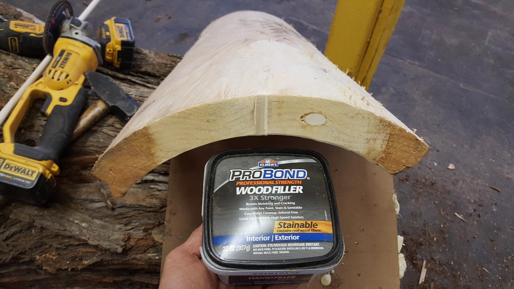 Elmer's ProBond Professional Strength Wood Filler 32oz held in front of the repaired IC WOOD half-log — stainable, interior/exterior, 3X stronger formula. DeWalt tools visible in background.